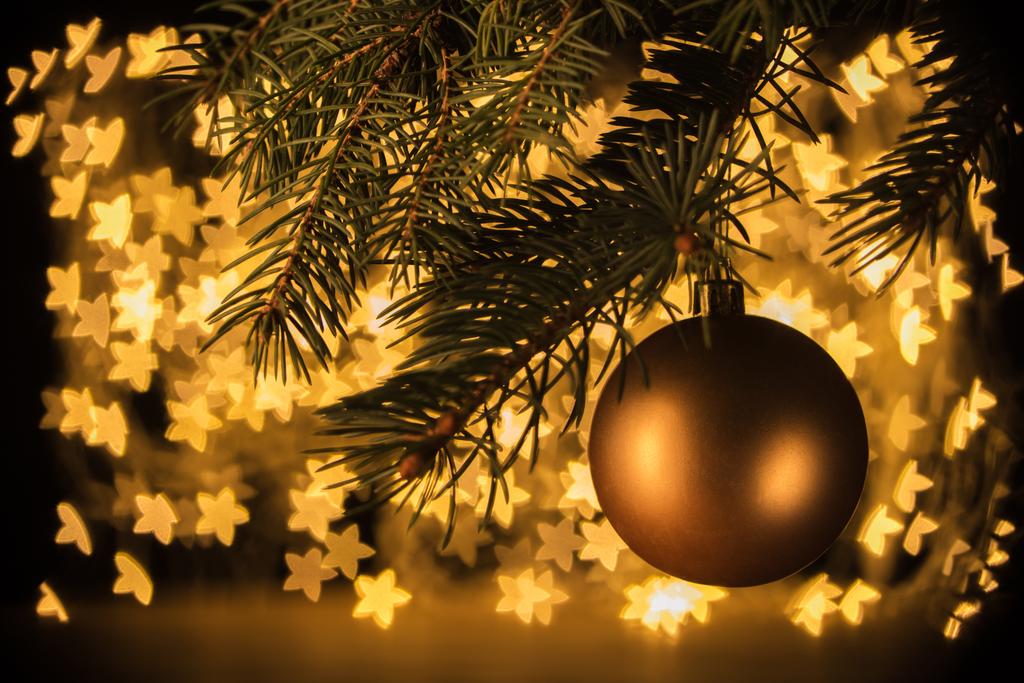 widok na złotą piłkę Bożego Narodzenia wisząca pine Tree z gwiazd bokeh świateł tło z bliska - Zdjęcie, obraz