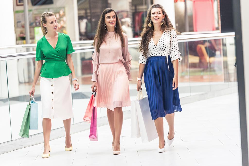 красивые улыбающиеся модные девушки с бумажными пакетами прогуливаясь по торговому центру
 - Фото, изображение