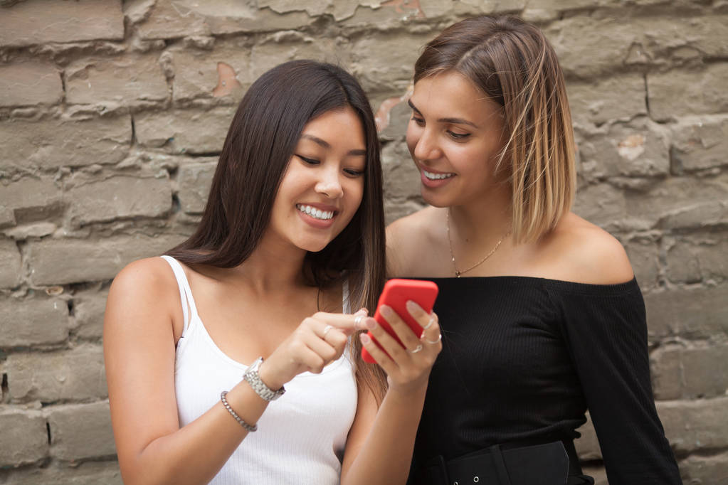 Две счастливые подруги делятся социальными сетями в смартфоне на улице в парке - Фото, изображение
