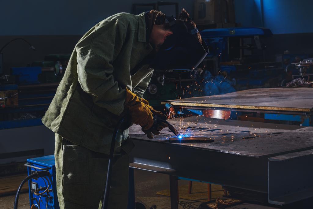 fabricación concentrada trabajador soldadura de metal con chispas en la fábrica
  - Foto, Imagen