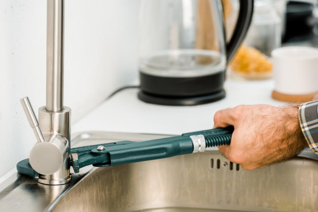 abgeschnittenes Bild von Klempner, der Wasserhahn mit Affenschlüssel in Küche repariert - Foto, Bild