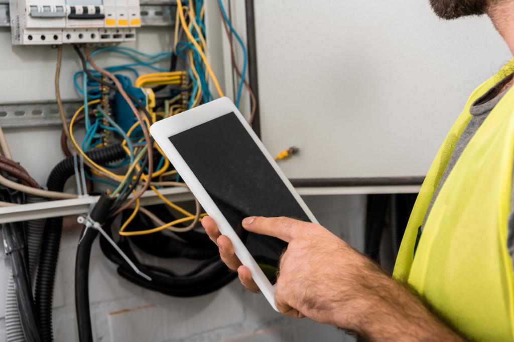 cropped image of electrician using tablet near electrical box in corridor - Photo, Image