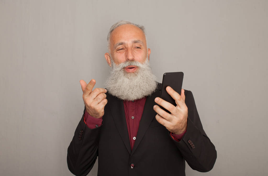 Photo studio d'un homme d'affaires barbu heureux souriant tout en utilisant un téléphone portable sur fond gris
 - Photo, image