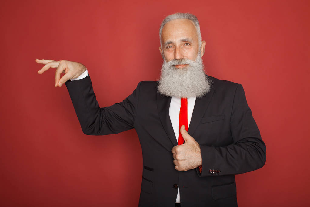 Bearded senior man smiling and holding something imaginary in one hand on red background - Photo, Image