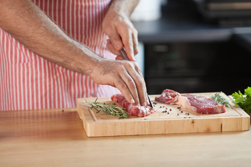 Kädet mies valmistaa lihaa ja vihanneksia keittiössä viipalointi vähärasvaista lihaa puulaudalla
. - Valokuva, kuva