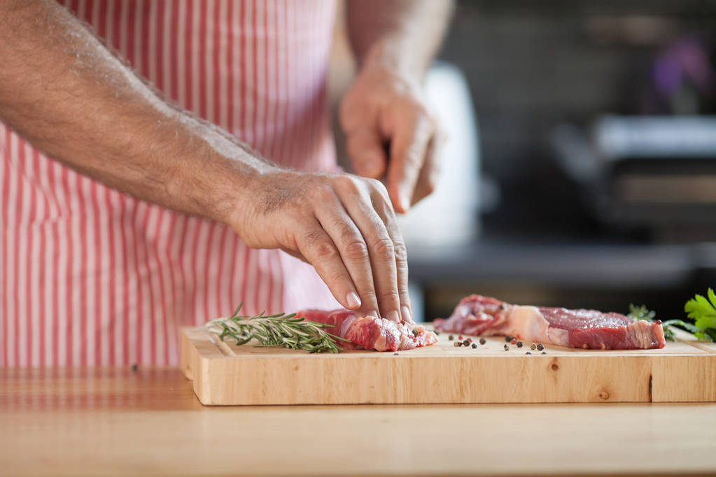 木の板に赤身の肉をスライス台所で肉や野菜を準備する男の手. - 写真・画像