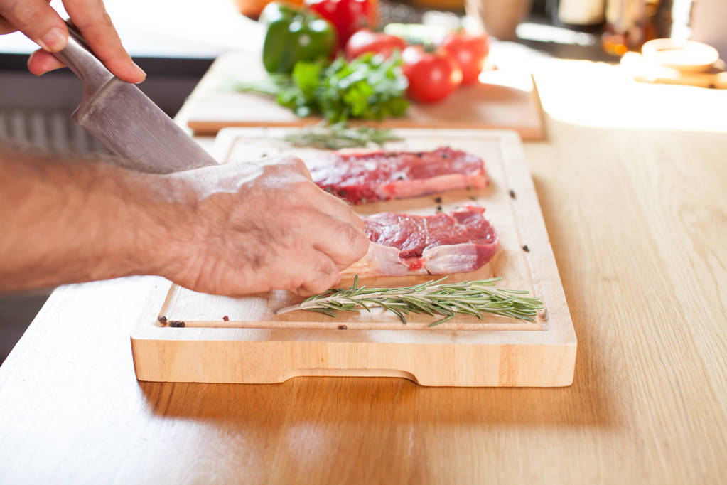 Rauwe biefstuk varkenshaas op een snijplank met rozemarijn peper zout vork en mes. - Foto, afbeelding