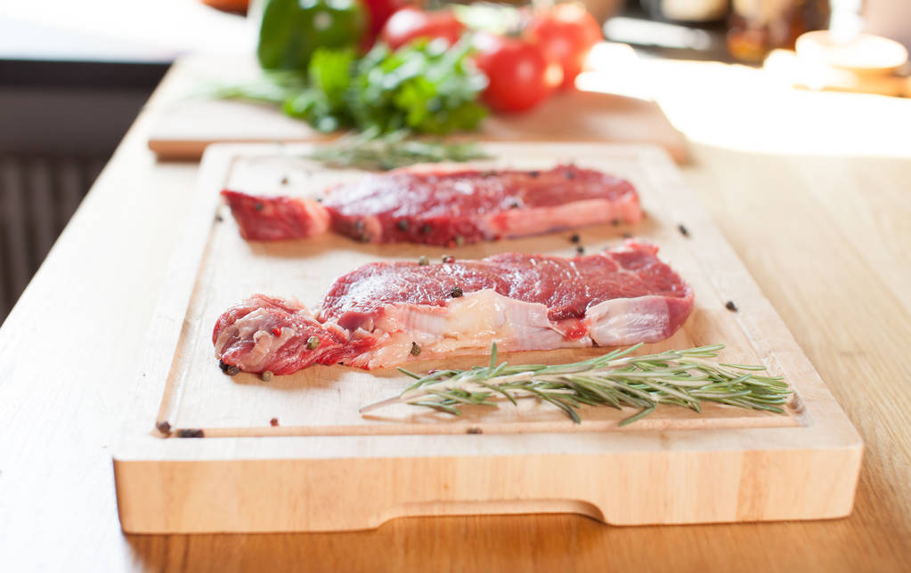 Rauwe biefstuk varkenshaas op een snijplank met rozemarijn peper zout vork en mes. - Foto, afbeelding