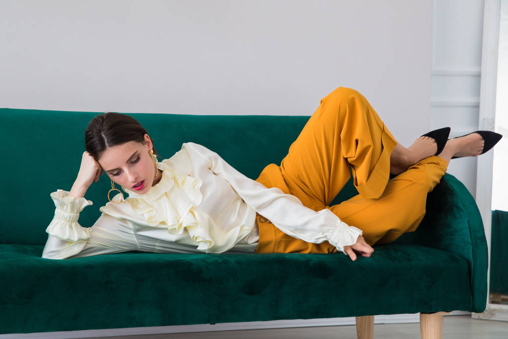 Красивая, серьезная, стильная молодая женщина, лежащая на диване в помещении
 - Фото, изображение