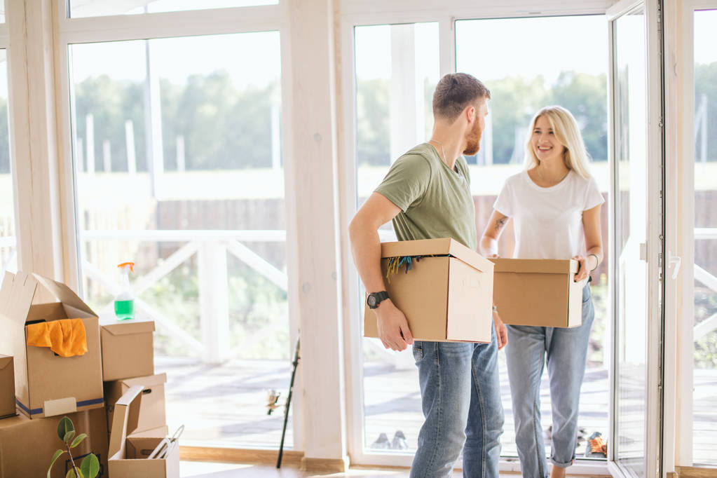 Couple heureux portant des boîtes en carton dans une nouvelle maison le jour du déménagement - Photo, image