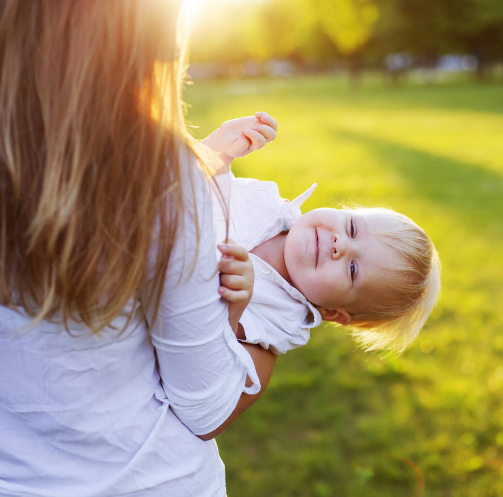 Ευτυχισμένη γυναίκα παίζει με τον γιο του νήπιο στο ηλιόλουστο πάρκο - Φωτογραφία, εικόνα
