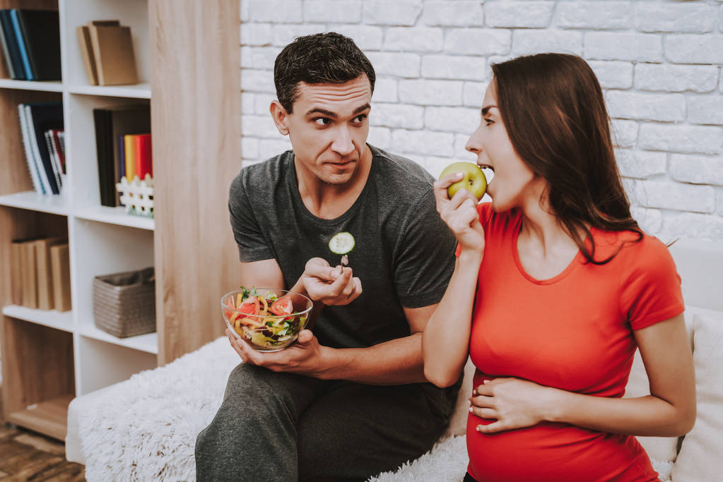 Husband and Pregnant Wife. Eat Apple. Salad. Freshness. Domestic Life. Parenthood. Happy Together. Natural Food. Apartment. Love Each Other. Home. Motherhood. Relaxation. Happiness. Birth. - Photo, Image