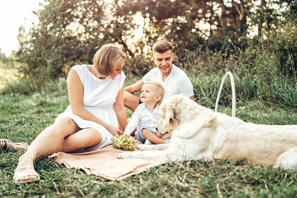 Joven bonita familia con perro relajante en el picnic en el prado
  - Foto, imagen