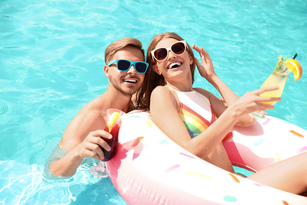 Молодая пара с коктейлями в бассейне в солнечный день
 - Фото, изображение