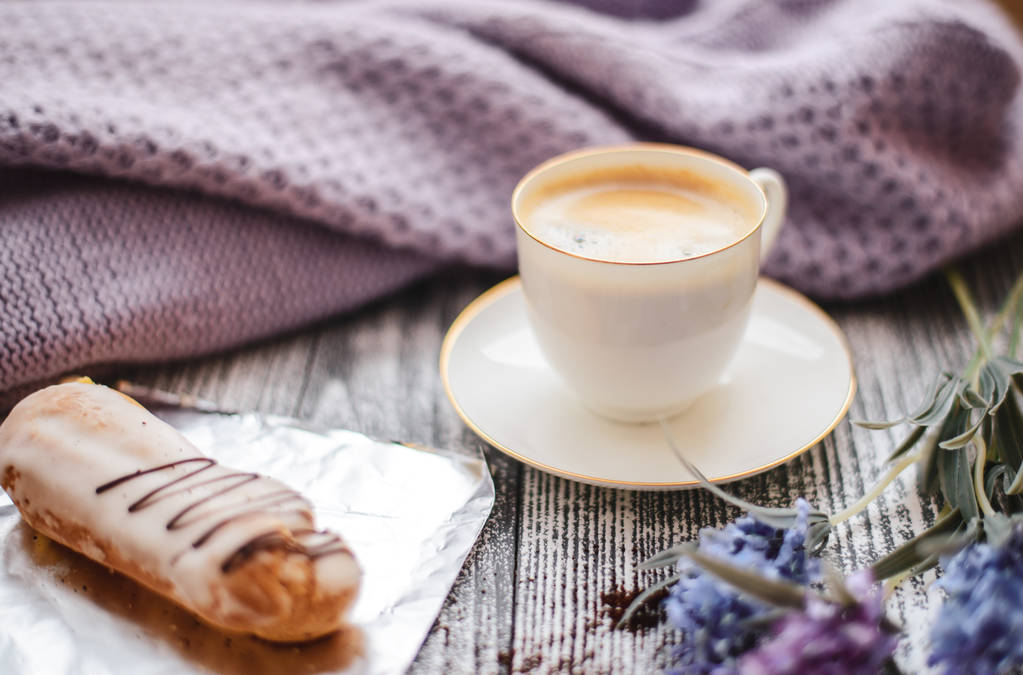 Šálek horké kávy, Eclair a květin na rustikální dřevěný stůl, detailní Foto Teplý svetr, zimní ráno koncepce, pohled shora. Ročník, tónovaná - Fotografie, Obrázek