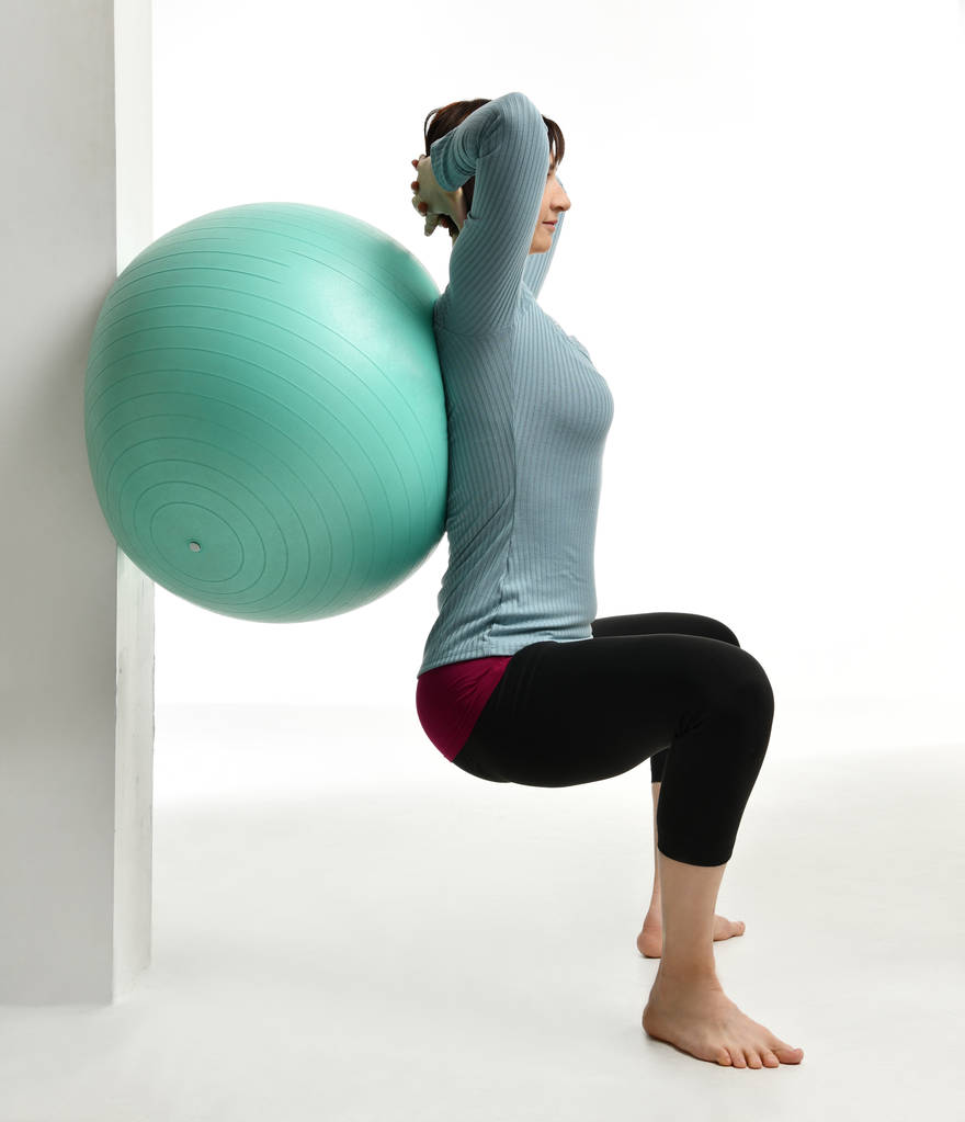 Female fitness instructor holds legs in gym and workout exercises for abdominals with green sport ball over white - Photo, Image