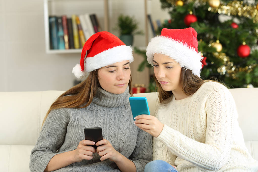 zwei Freunde, die an den Weihnachtsfeiertagen telefonieren und zu Hause auf einer Couch im Wohnzimmer sitzen - Foto, Bild