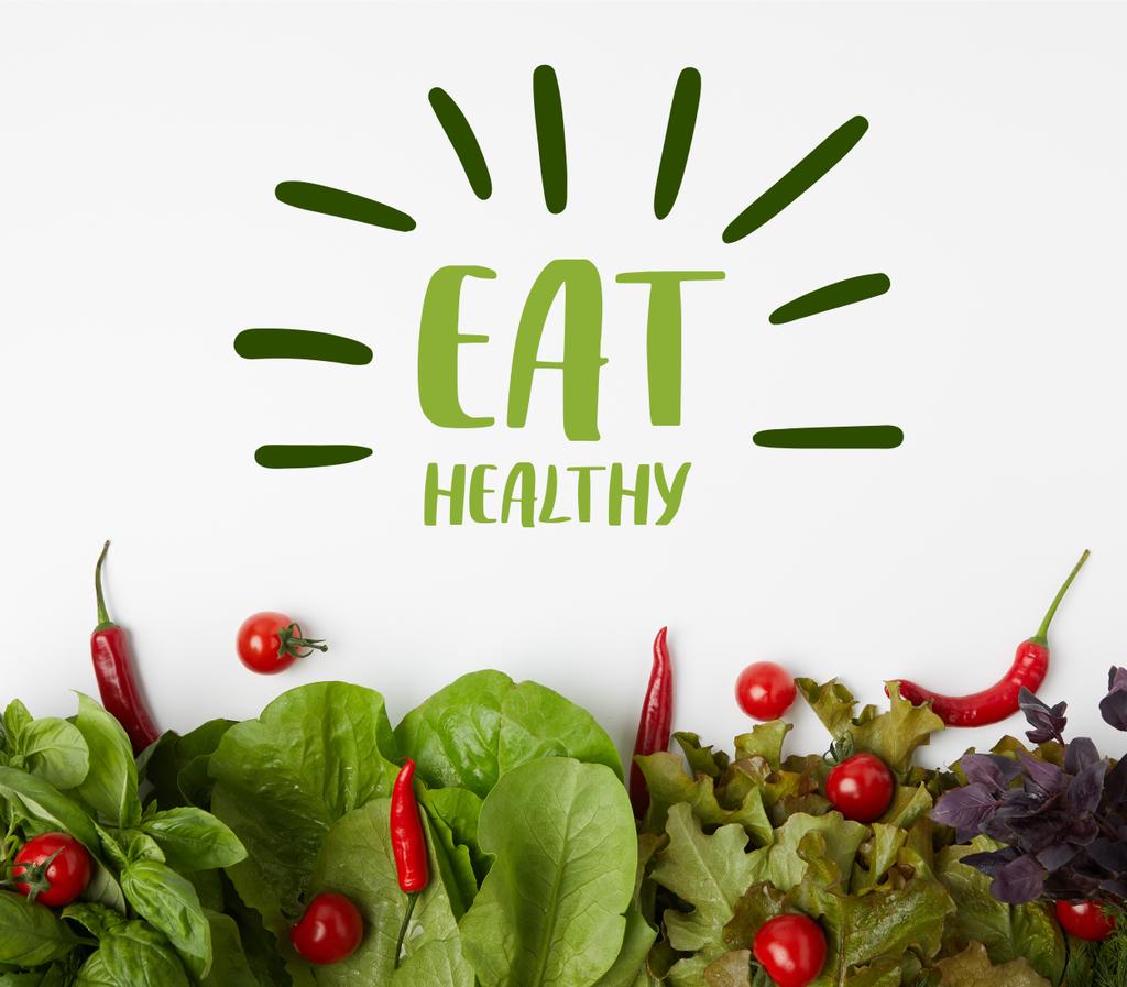 pohled shora čerstvého různé listová zelenina s rajčaty a paprikami na bílém povrchu s nápisem "jíst zdravě" - Fotografie, Obrázek