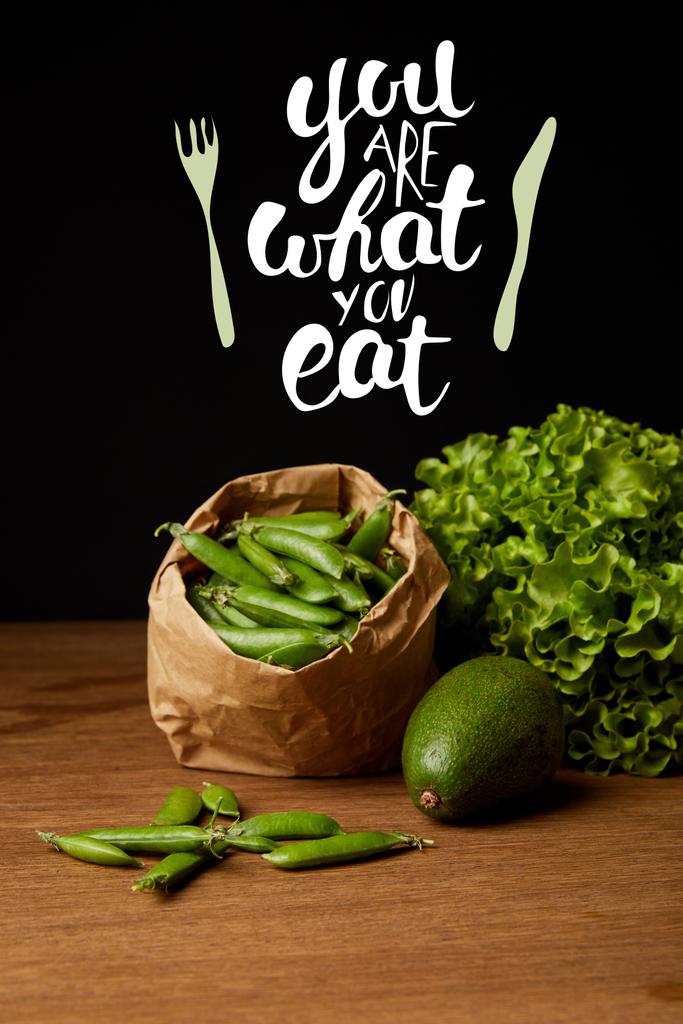 Close-up shot van avocado, groene erwten en sla op houten oppervlak met "je bent wat je eet" inspiratie - Foto, afbeelding