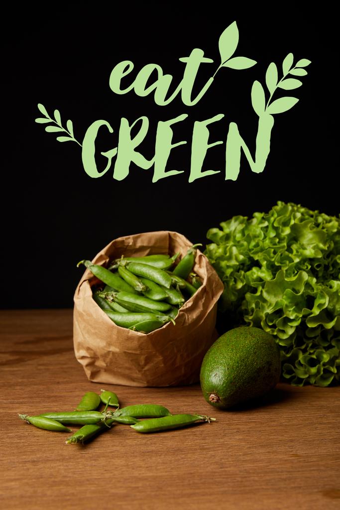 Close-up shot van avocado, groene erwten en sla op houten oppervlak met "eet de groene" belettering - Foto, afbeelding