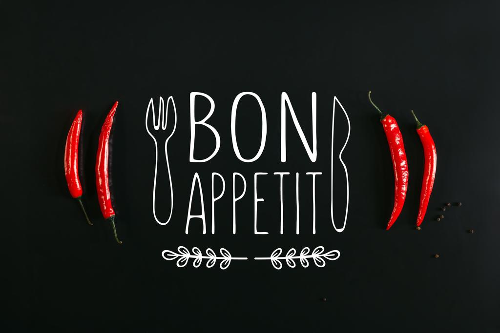 ナイフとフォークの「ボナペティ」のレタリングと黒の背景に赤唐辛子と胡椒のトップ ビュー - 写真・画像
