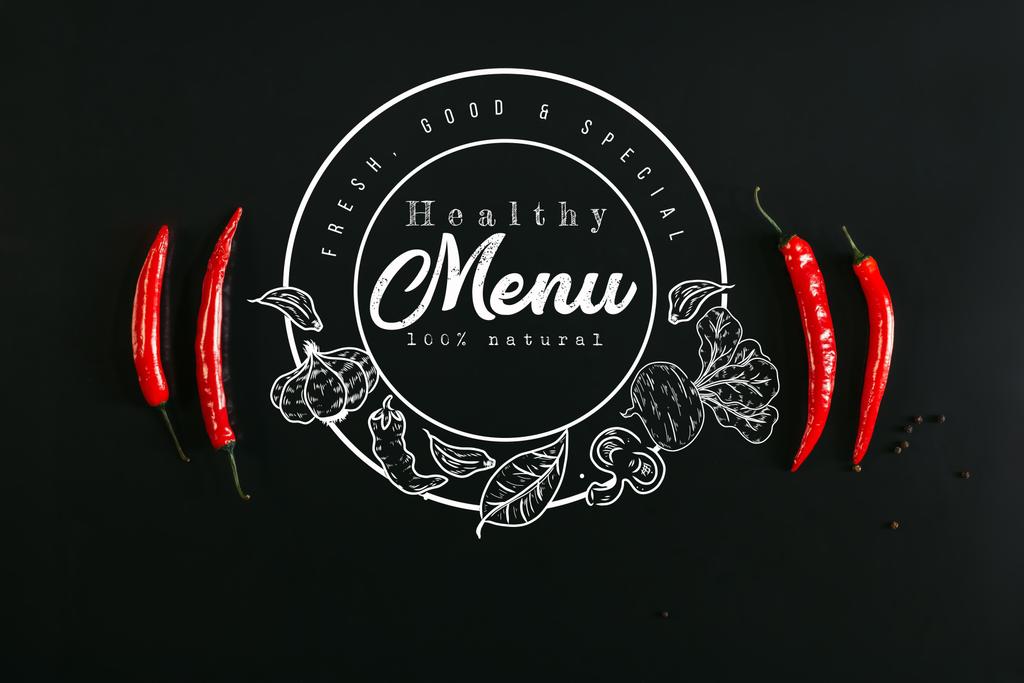 top view of red chili peppers and peppercorns on black background with "healthy menu" lettering in seal - Photo, Image