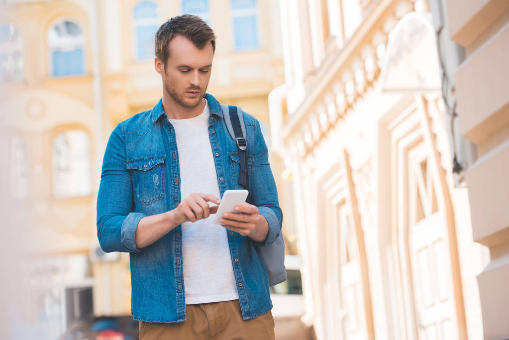 portrait of focused man in denim shirt using smartphone on street - Photo, Image