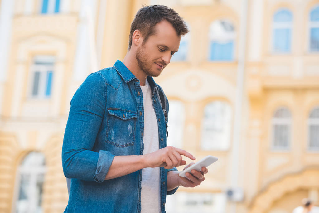 Вид сбоку человека в джинсовой рубашке с помощью смартфона на улице
 - Фото, изображение