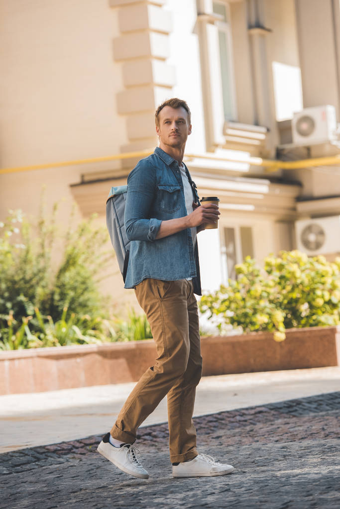 yakışıklı genç adam kahve ile gitmek ve şehir tarafından yürüyüş ve uzak seyir sırt çantası - Fotoğraf, Görsel
