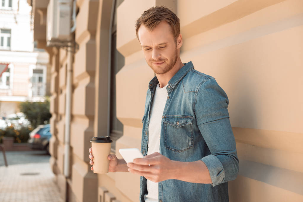 handsome young man with coffee to go using smartphone on street - Photo, Image