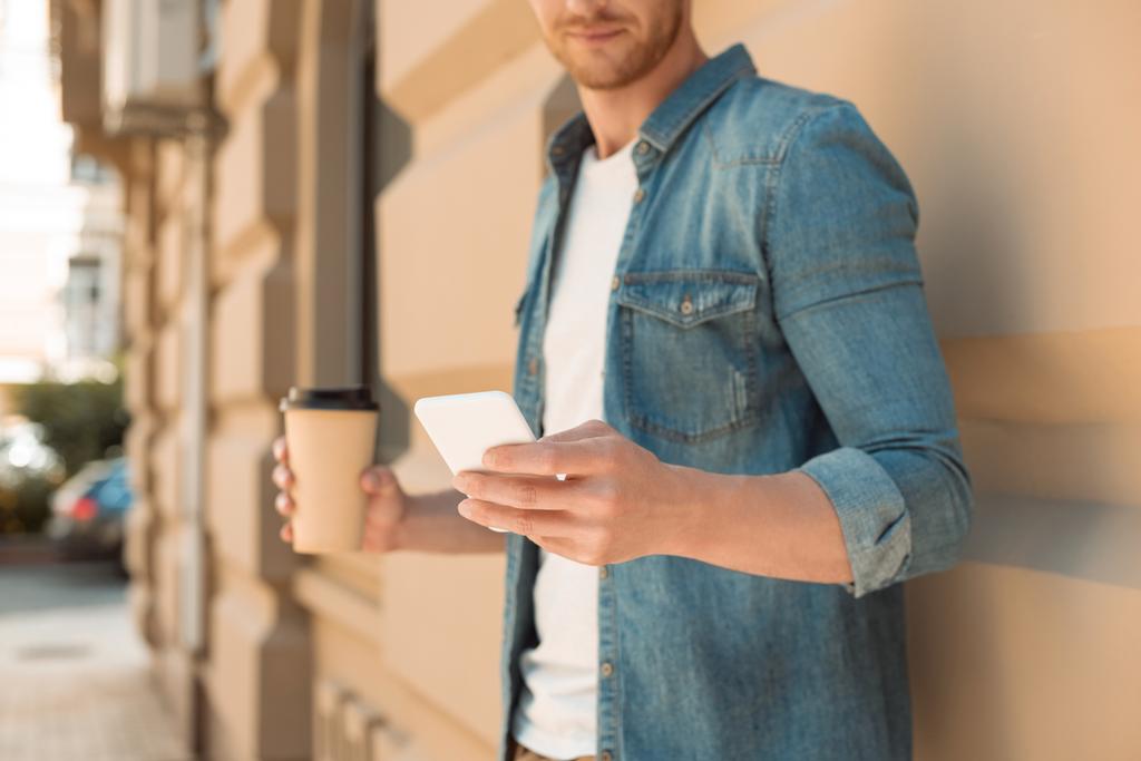 plan recadré de jeune homme avec du café pour aller à l'aide d'un smartphone dans la rue
 - Photo, image