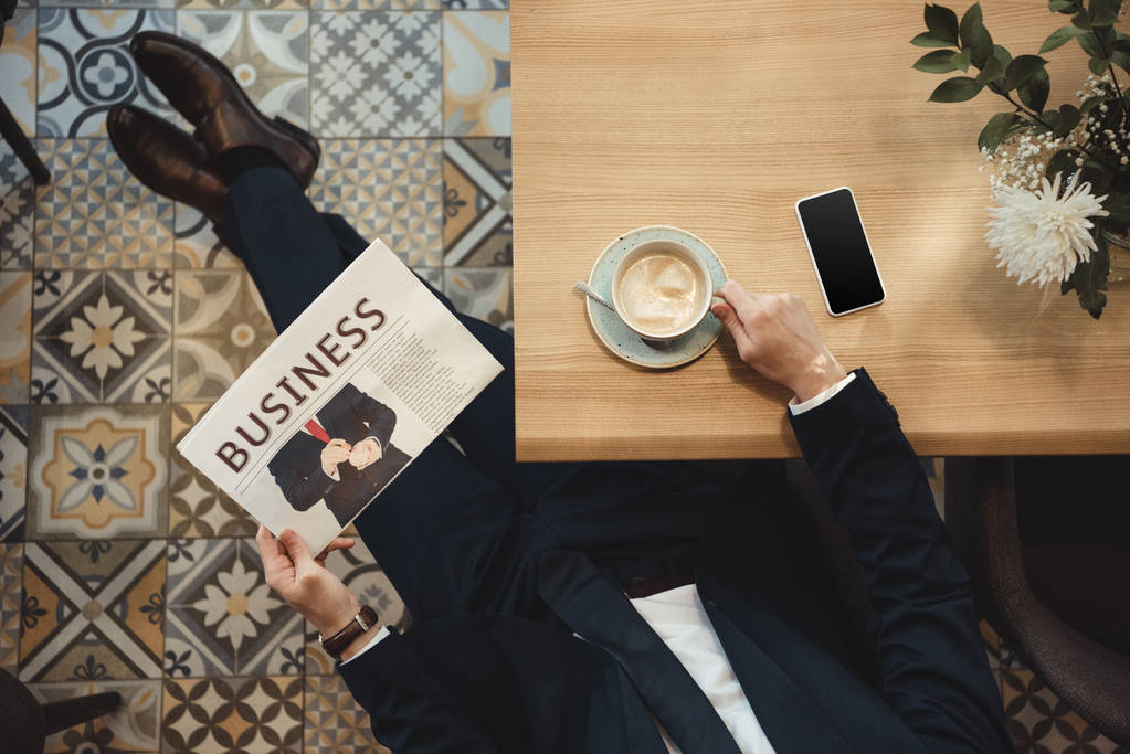 vista aérea del hombre de negocios en traje con periódico en la mesa con taza de café y teléfono inteligente en la cafetería
 - Foto, imagen
