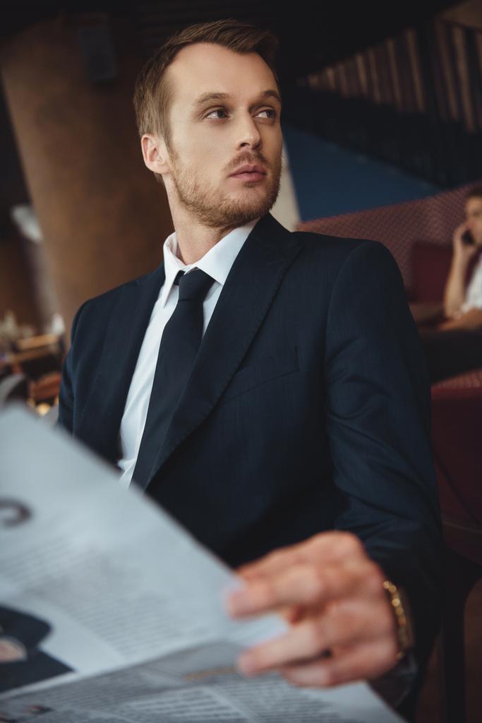 uomo d'affari in abito nero con giornale guardando altrove nel caffè
 - Foto, immagini
