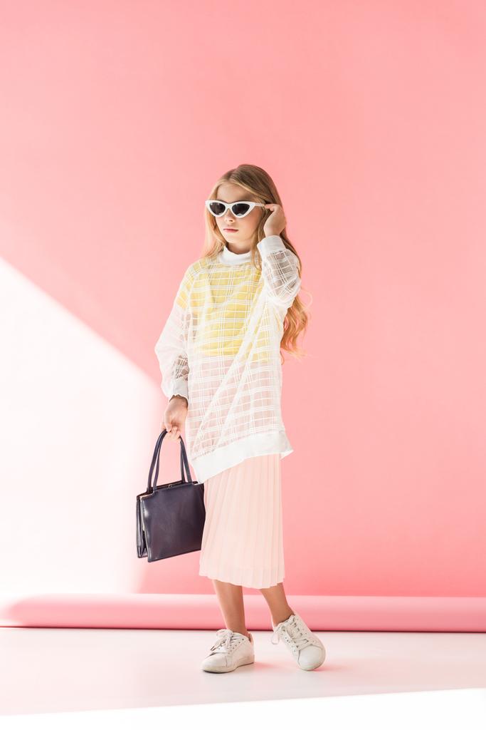 блондинка модна молодша в сонцезахисних окулярах позує з мішком на рожевому
 - Фото, зображення