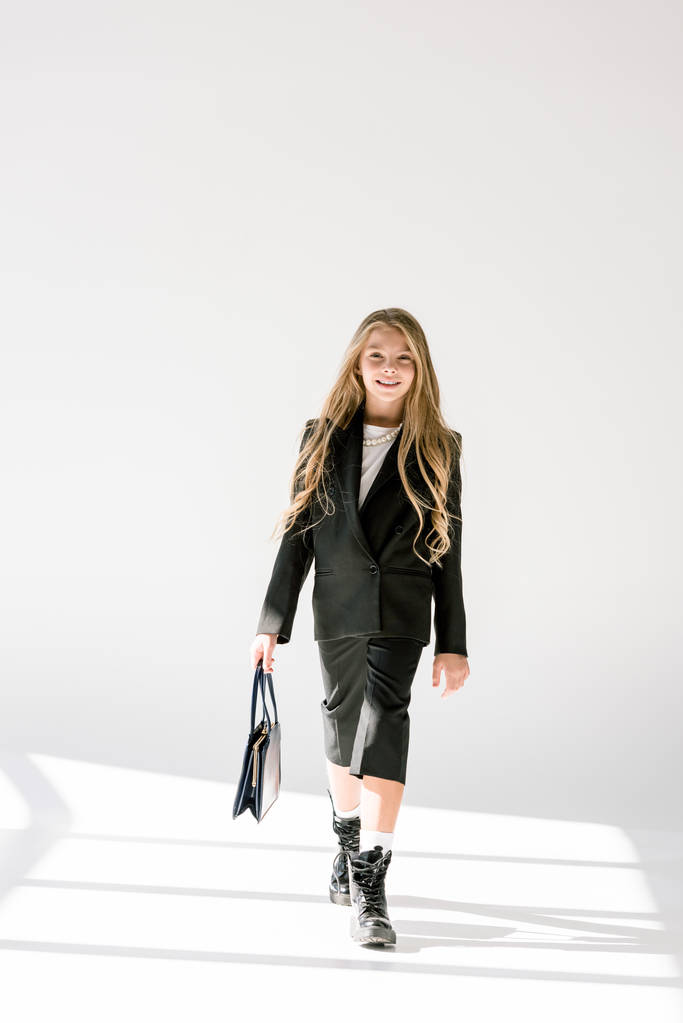 fashionable smiling child in black suit posing with bag on grey - Photo, Image