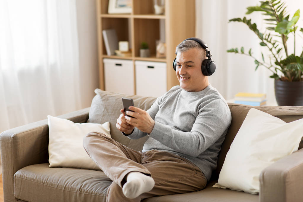 άνθρωπος με smartphone και ακουστικά στο σπίτι - Φωτογραφία, εικόνα