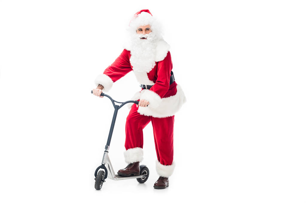 santa claus in costume standing with kick scooter and looking away isolated on white background - Photo, Image