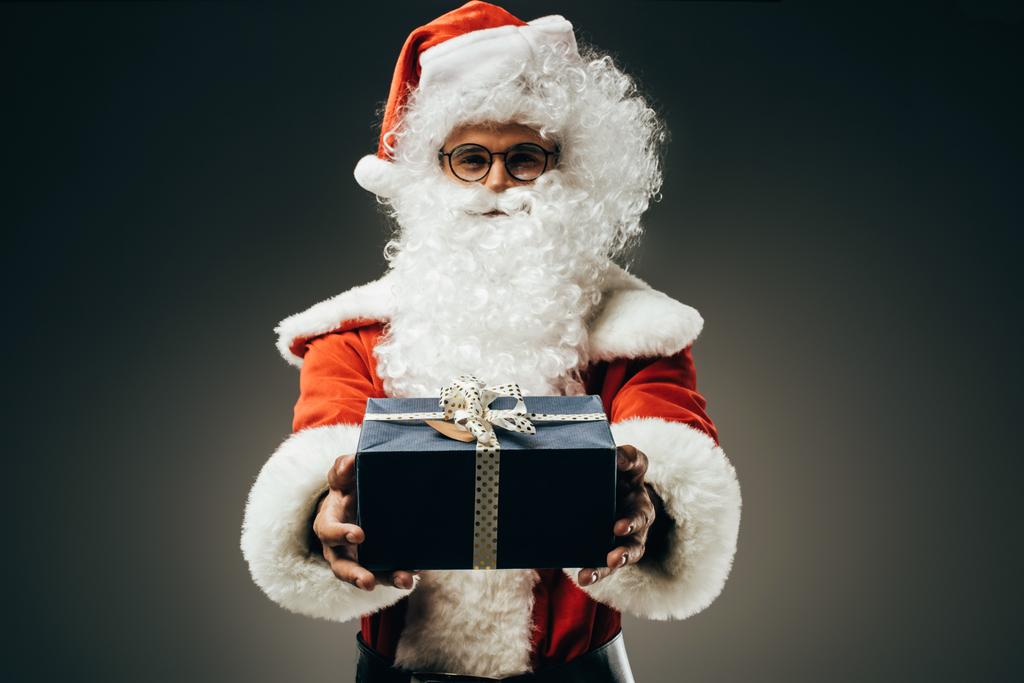 усміхнений Санта Клаус в костюмі, що показує подарункову коробку ізольовано на сірому фоні
  - Фото, зображення