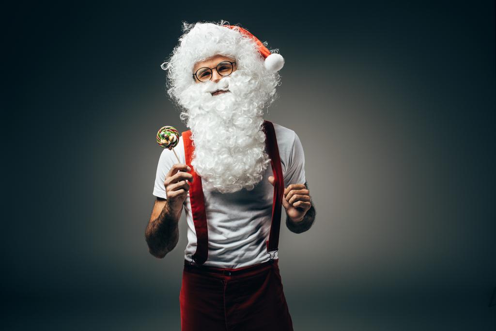 neşeli Noel Baba'ya izole gri arka plan üzerinde renkli lolipop ile ayakta gözlük  - Fotoğraf, Görsel