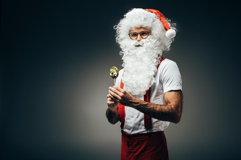 mutlu Noel Baba'ya izole gri arka plan üzerinde renkli lolipop ile ayakta gözlük  - Fotoğraf, Görsel