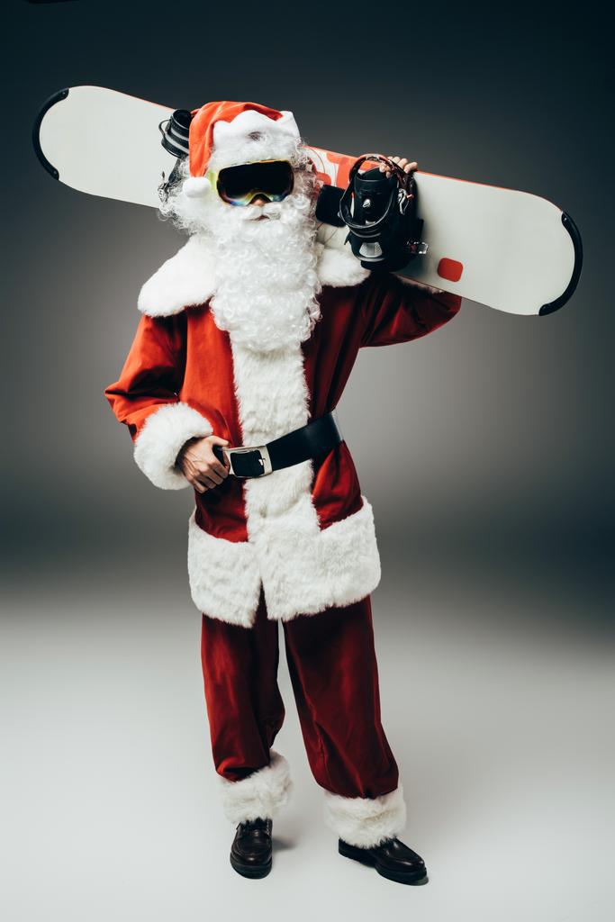 Noel Baba'ya kar maskesi gri arka plan üzerinde omuz üzerinden snowboard holding  - Fotoğraf, Görsel