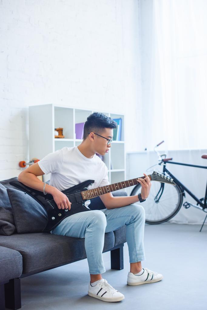 όμορφος Ασίας άντρας παίζει μείζονα συγχορδία F στο unplugged ηλεκτρική κιθάρα στο σπίτι - Φωτογραφία, εικόνα