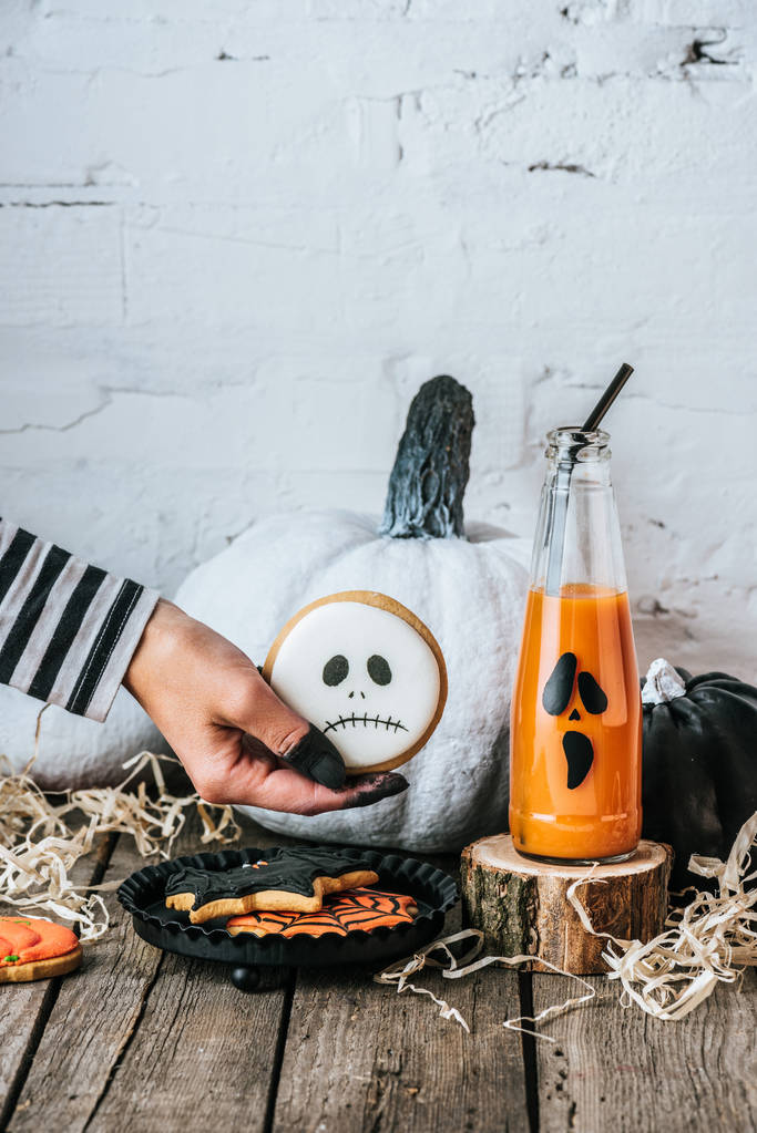 oříznutý snímek ženy držící cookie halloween dýně a šťávu na dřevěný povrch - Fotografie, Obrázek