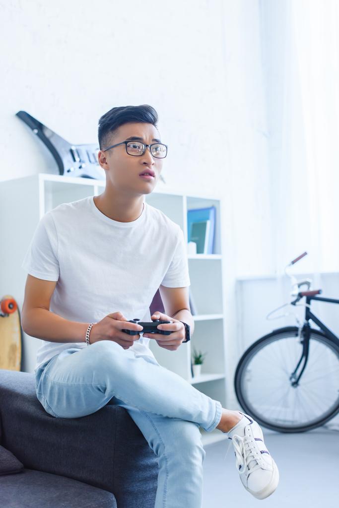 upset handsome asian man playing video game on sofa at home - Photo, Image