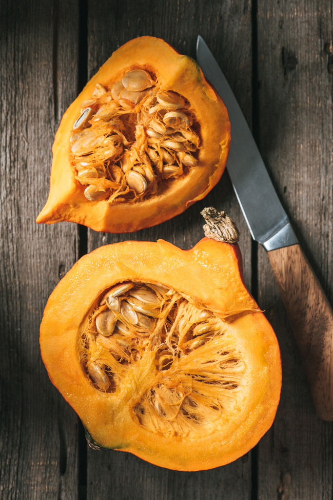 Flat lay with knife and raw pumpkin halves on wooden background - Photo, Image