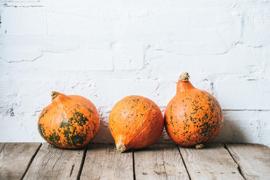 close up view of arranged ripe pumpkins on wooden tabletop and white brick wall backdrop - Photo, Image