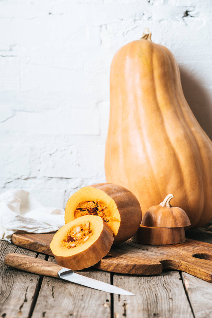 close up view of ripe pumpkins and knife on wooden planks surface and white brick wall background - Photo, Image
