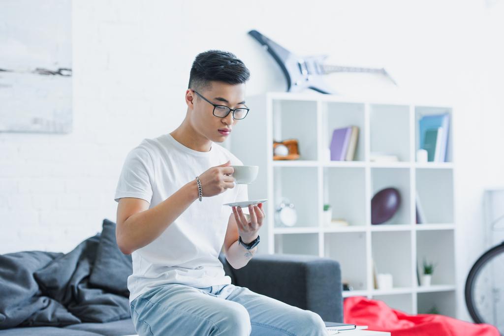 красивий азіатський чоловік сидить на столі з чашкою кави вранці вдома
 - Фото, зображення