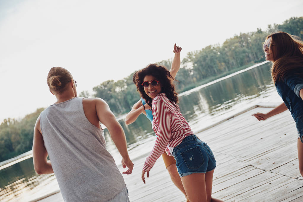 ευτυχισμένοι άνθρωποι διασκεδάζουν και τρέχει σε ξύλινη προβλήτα στον ποταμό  - Φωτογραφία, εικόνα