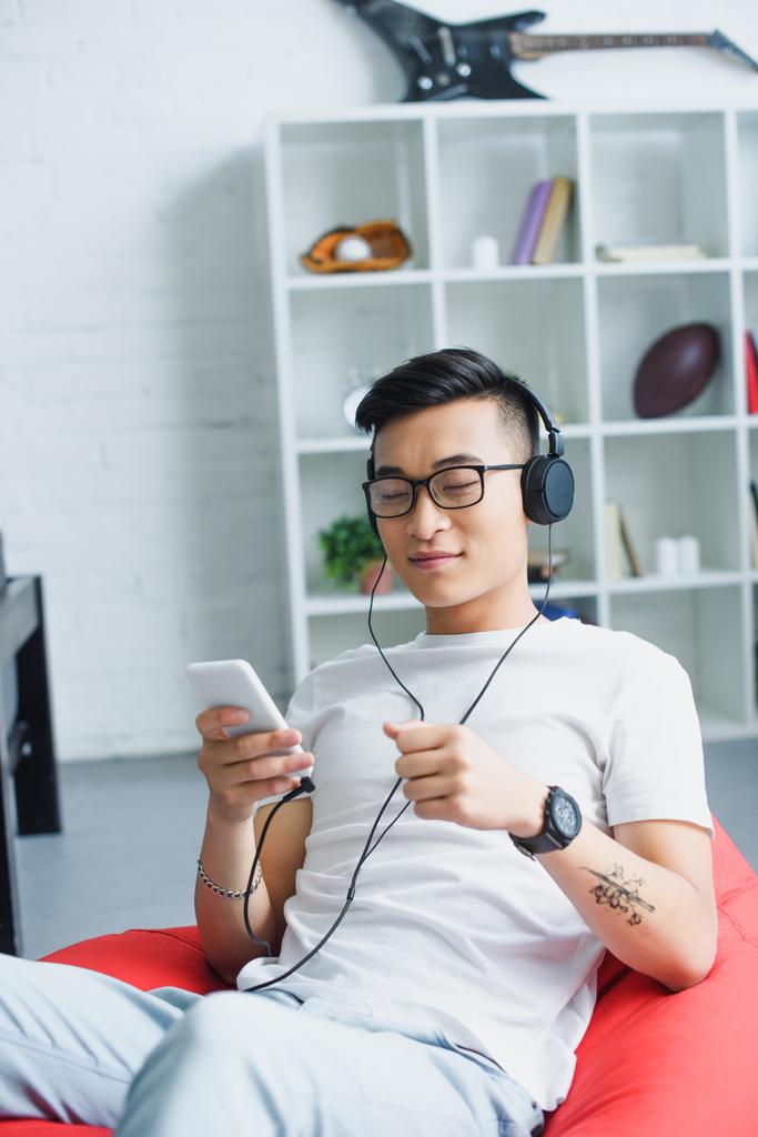 красивый молодой азиат, использующий смартфон и слушающий музыку в наушниках
 - Фото, изображение